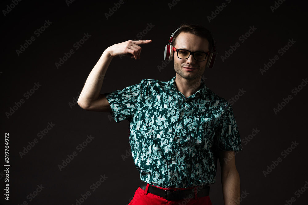 fashionable man in eyeglasses pointing with finger at headphones isolated on black fashionable man in eyeglasses pointing with finger at headphones isolated on black