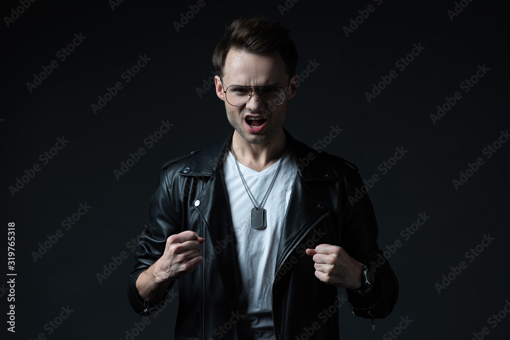 angry stylish brutal man in biker jacket showing fists isolated on black