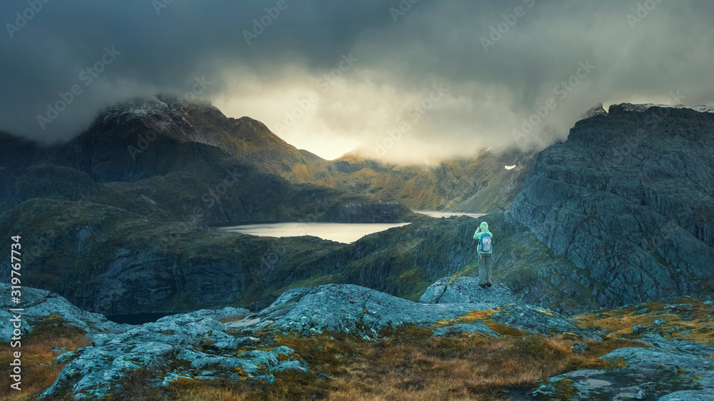 tourist photographs gaps of sunlight among thunderclouds on a trek on Mount Munken in Norway on the Lofoten Islands