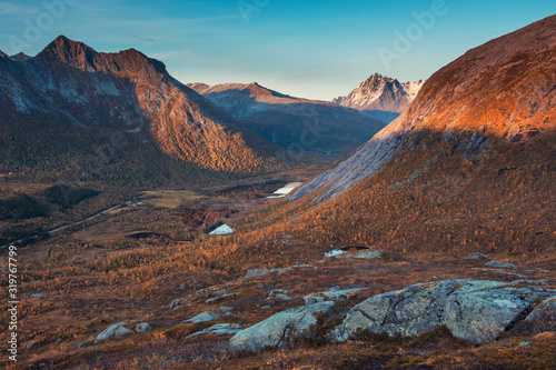 Evening autumn landscape with sunset light in the mountains of Norway on the Lofoten islands. Lakes and Yellow Forest at the foot of hills and snowy peak