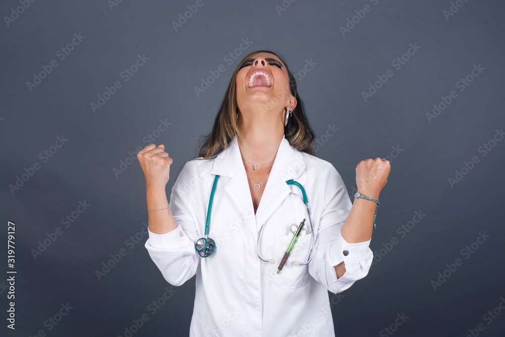 Portrait of beautiful doctor female looks with excitement up, keeps hands raised, notices something unexpected, poses indoors. Lovely woman reacts on sudden news Portrait of beautiful doctor female looks with excitement up, keeps hands raised, notices something unexpected, poses indoors. Lovely woman reacts on sudden news