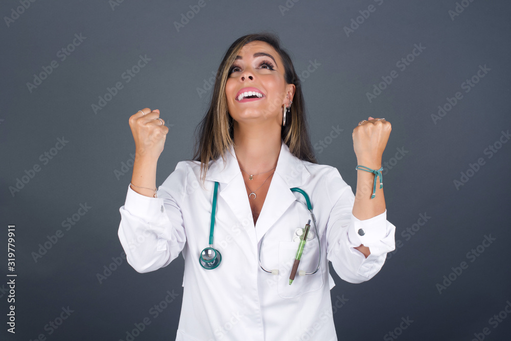 Excited young doctor woman winner raising fists with great happiness having good mood after winning game. Young champion having success being glad to achieve her goals. Victory and triumph concept. Excited young doctor woman winner raising fists with great happiness having good mood after winning game. Young champion having success being glad to achieve her goals. Victory and triumph concept.
