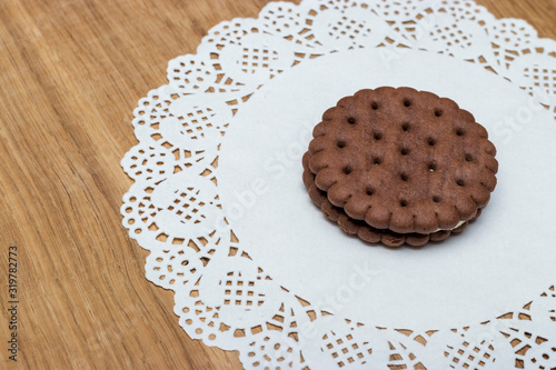 A round shortbread biscuit with cream lies on a paper napkin with beautiful lace edges. Dessert for tea or coffee, children's treat.