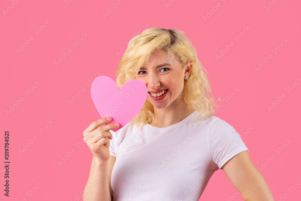 Studio portrait of a smiling young woman holding pink heart, romantic love, dating and Valentine's Day concept Studio portrait of a smiling young woman holding pink heart, romantic love, dating and Valentine's Day concept