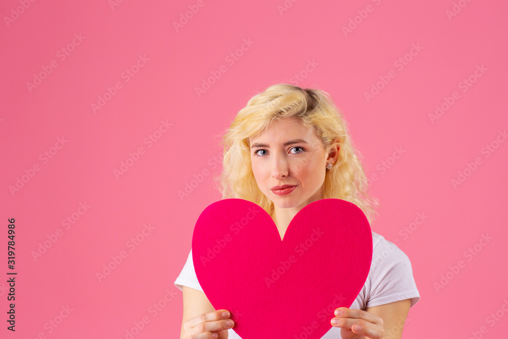 Studio portrait of a young blonde model holding pink heart, romantic love, dating and Valentine's Day concept