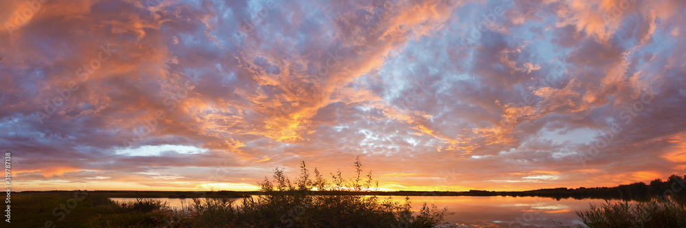 Panorama of bright colorful sunset on the background of yellow-red clouds reflected in water of lake