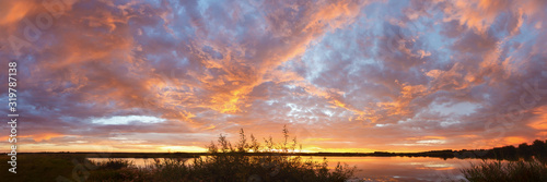 Panorama of bright colorful sunset on the background of yellow-red clouds reflected in water of lake