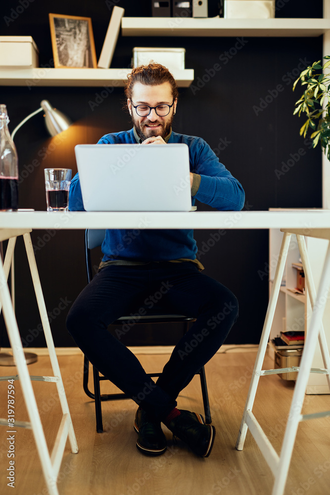 Fototapeta premium Handsome caucasian bearded businessman sitting in his modern office and using laptop for writing report.