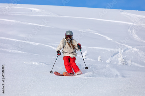 Girl On the Ski. a skier in a bright suit and outfit with long pigtails on her head rides outside of the track with swirls of fresh snow. ski freeride, downhill in sunny day. Heliboarding skiing photo