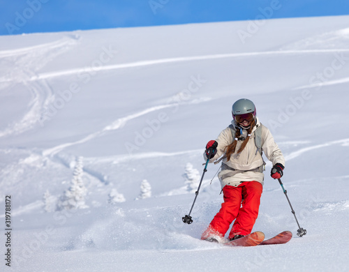 Girl On the Ski. a skier in a bright suit and outfit with long pigtails on her head rides outside of the track with swirls of fresh snow. ski freeride, downhill in sunny day. Heliboarding skiing