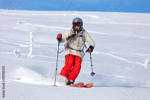 Girl On the Ski. a skier in a bright suit and outfit with long pigtails on her head rides outside of the track with swirls of fresh snow. ski freeride, downhill in sunny day. Heliboarding skiing photo