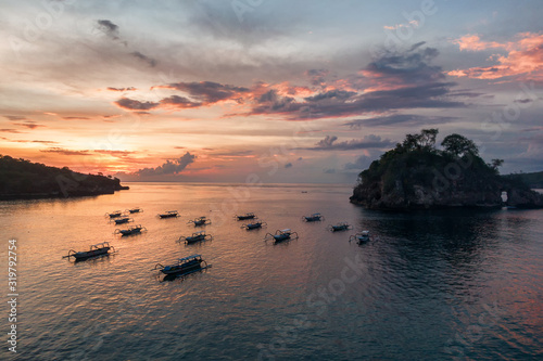 Aerial of Longtail boats moored in Crystal Bay  Nusa Penida  with island silhouette and amazing sunset in the background