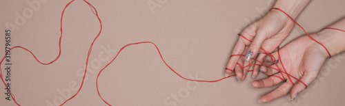 Top view of female hands with red string on beige background  panoramic shot