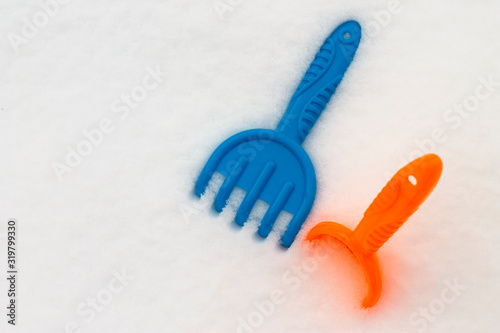 Children's toys in the snow. Plastic blue rake of children in the snow and a yellow shovel.