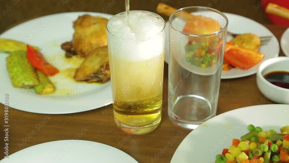 Foamy light beer from a bottle is poured into a transparent glass