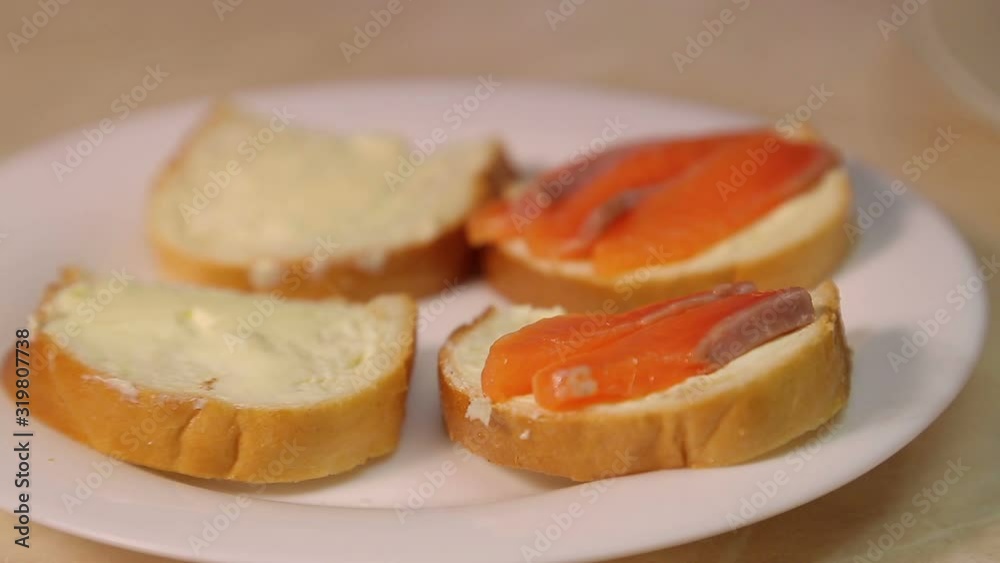 Female hand puts slices of red fish on sandwiches with butter Female hand puts slices of red fish on sandwiches with butter