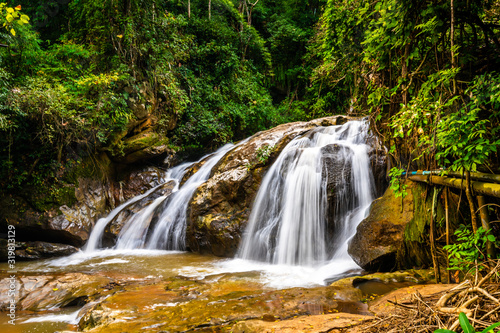 Beautiful waterfall Mae Sa, Thailand. Fresh and pure water stream is flowing on the rock stone ground in tropical rainforest. Fresh plants and trees above river. Vibrant colors in pure nature