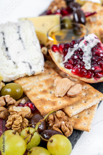 Food Platter With Truffle Cheese, Duck Breast, Brie Cheese, Pecan Nuts, Pomegranate Seeds, Grapes, Almonds, Honey, Olives and Crackers on White Marble Background
