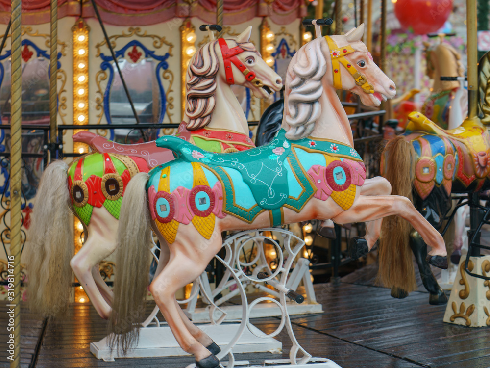 Colorful vintage merry-go-round wooden horses. Photography of the city amusement park. Downtown buildings as background. Concepts of fun and childhood.