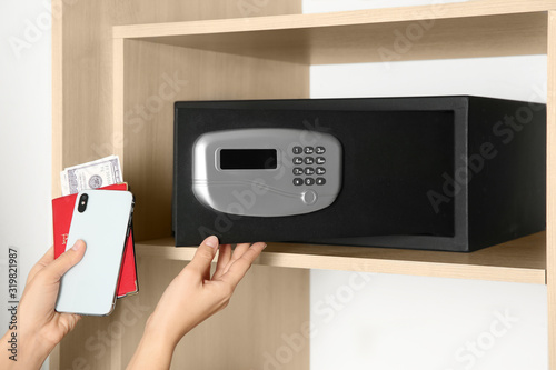 Woman putting smartphone, passport and money into steel safe, closeup