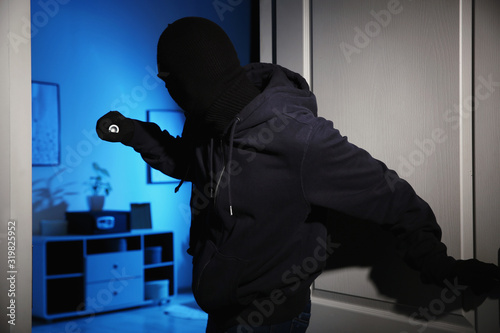 Tablou pe pânză Thief with flashlight breaking into house at night