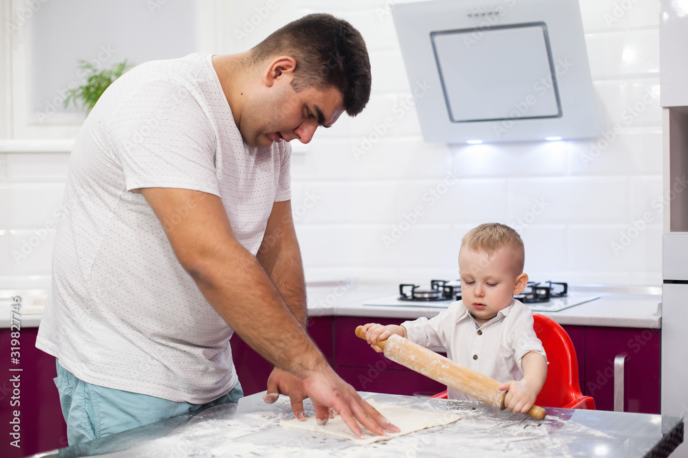 Obraz premium Kid rolls out the pizza dough. Happy family in kitchen.