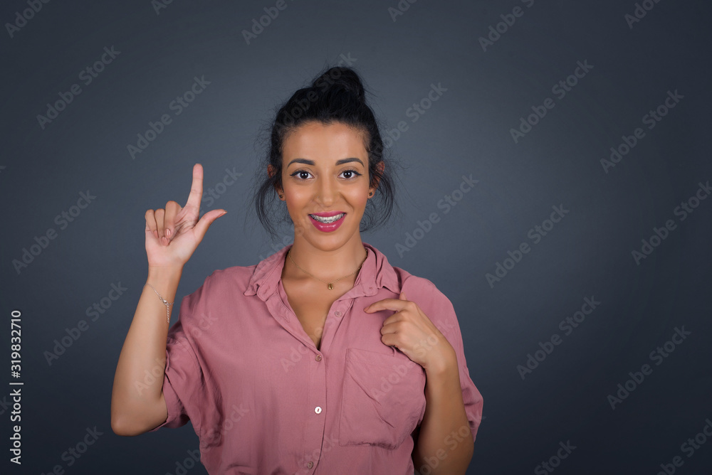 Positive glad female says: wow how exciting it is, has amazed expression, indicates something. Joyful pretty young woman demonstrates something. One hand on her chest and pointing with other hand. Positive glad female says: wow how exciting it is, has amazed expression, indicates something. Joyful pretty young woman demonstrates something. One hand on her chest and pointing with other hand.