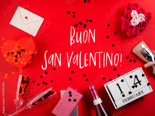 Fotografija Happy valentines day concept flat lay with champagne flutes and red heart confetti on red background, wooden calendar, envelope, heart shaped gift box