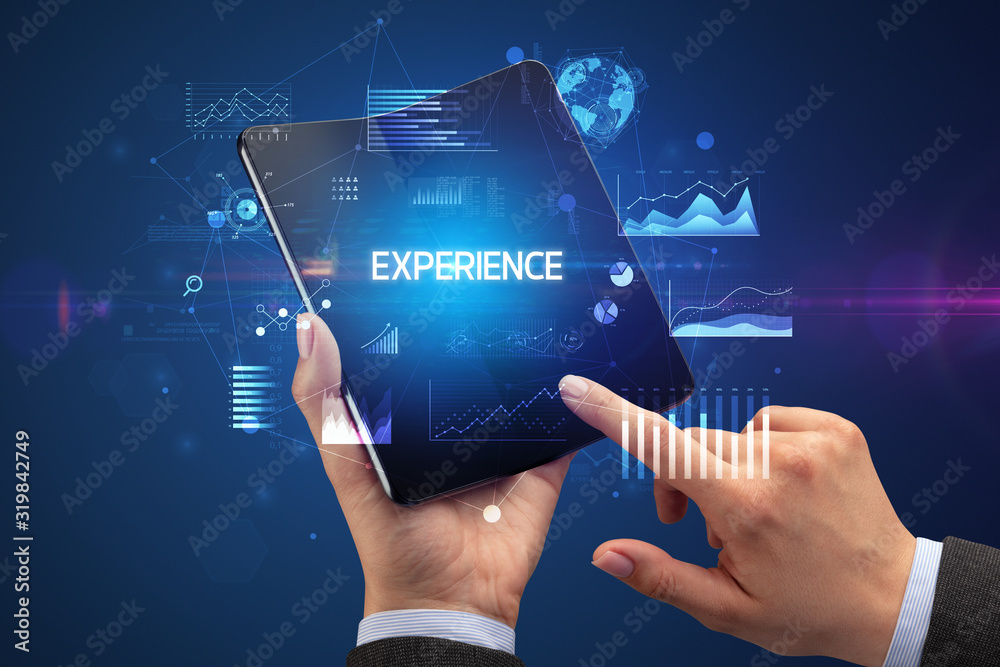 Businessman holding a foldable smartphone with EXPERIENCE inscription, successful business concept Businessman holding a foldable smartphone with EXPERIENCE inscription, successful business concept