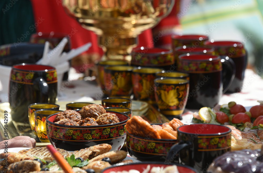Set of tea cups with Russian traditional ornament on the table with samovar and fish dishes