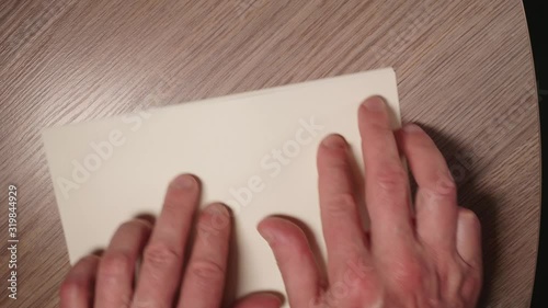 Close up and up view of man's hands fold white sheet of paper in half to leave a message.