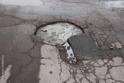 one large pothole with white ice on a gray asphalt road with cracks in a frosty winter day