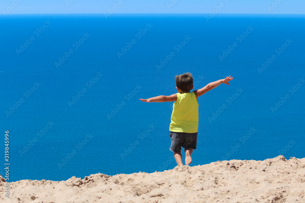 Young male caucasian preschooler jumping from a sandhill into a perfect blue sea. Young male caucasian preschooler jumping from a sandhill into a perfect blue sea.