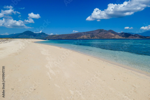 A view on white sand beach on a small island near Maumere  Indonesia. Happy and careless moments. Waves gently washing the shore. Clear  turquoise coloured water displaying coral reef. Hidden gem.