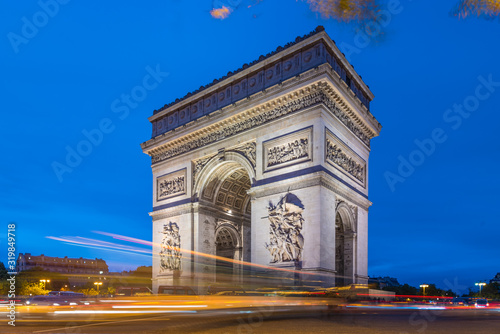 Arc de Triomphe at dusk in Paris in France with traffic of cars light trails and yellow leafs moved by the wind