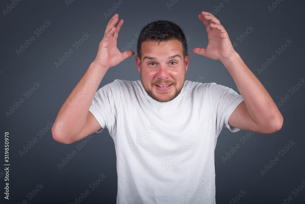 Portrait of handsome male looks with excitement at camera, keeps hands raised over head, notices something unexpected, isolated over gray wall. Lovely man reacts on sudden news. Portrait of handsome male looks with excitement at camera, keeps hands raised over head, notices something unexpected, isolated over gray wall. Lovely man reacts on sudden news.