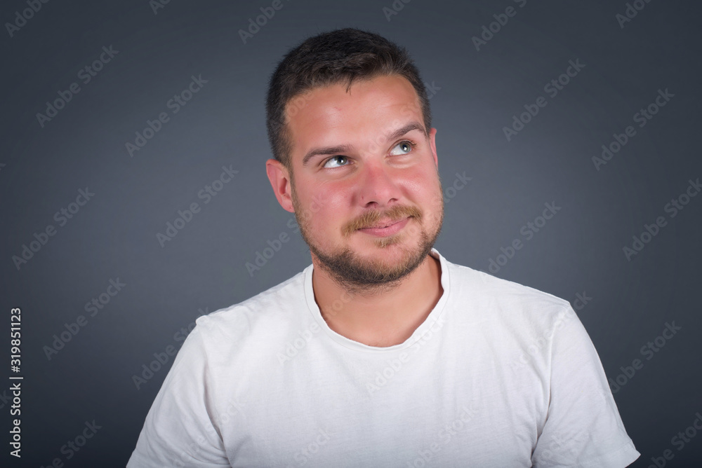 Gloomy, wondering young man face looking up lips together, being upset thinking about something important, keeps hands down, man standing indoors. Gloomy, wondering young man face looking up lips together, being upset thinking about something important, keeps hands down, man standing indoors.