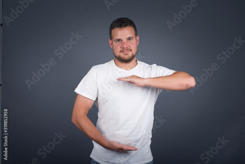 Young handsome young man wearing casual clothes over isolated background gesturing with hands showing big and large size sign, measure symbol. Smiling looking at the camera. Measuring concept.