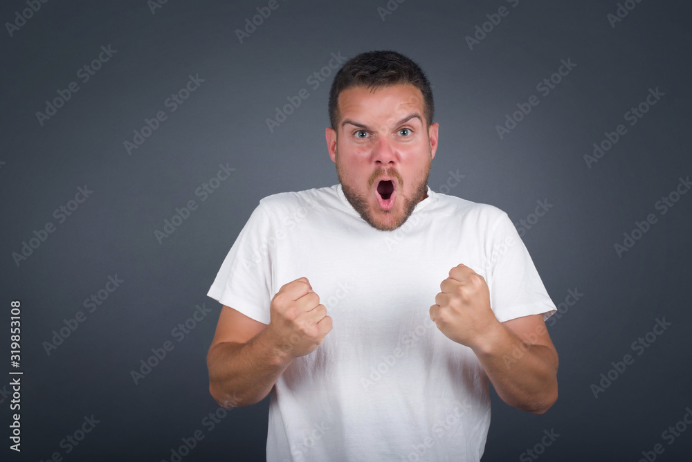Waist up portrait of strong successful determined young male winner in casual clothes raising arms, clenching fists, exclaiming GOAL with joy and excitement. Victory, success and achievement concept. Waist up portrait of strong successful determined young male winner in casual clothes raising arms, clenching fists, exclaiming GOAL with joy and excitement. Victory, success and achievement concept.