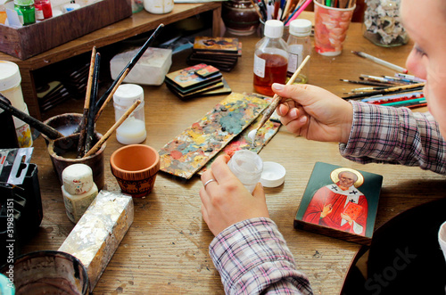 For protection wooden picture is process of applying сraquelure varnish on the product. Reproduction of the icon of St. Nicholas. Workflow of the artist in the studio. Brushes and paints. photo