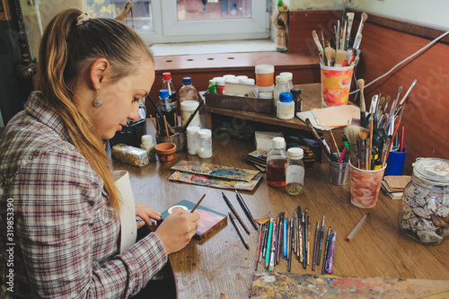 Girl artist paints a picture in the studio. Reproduction of the icon of St. Nicholas. Workflow of the artist in the studio. Brushes and paints on the background art workplace. photo