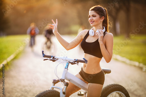 joyful girl with a beautiful figure holds headphones and sits on a bicycle at sunset in the park
