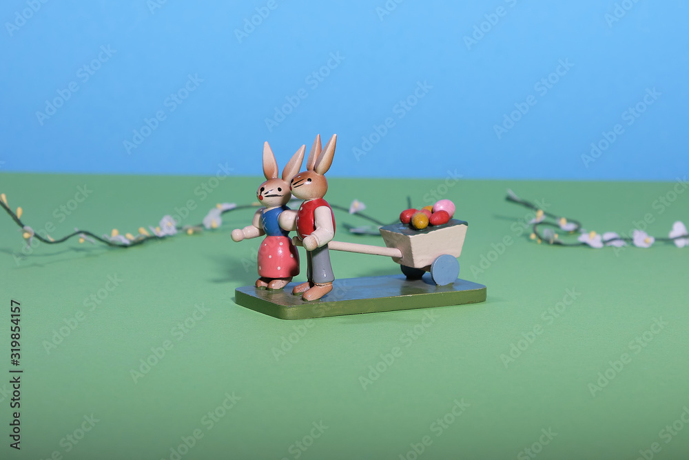 Fototapeta premium Two easterbunnies pull a cart with coloured eggs