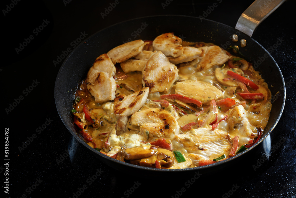Cooking a creamy chicken ragout with bell pepper and mushroom in a pan on a black stove, copy space Cooking a creamy chicken ragout with bell pepper and mushroom in a pan on a black stove, copy space