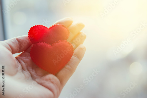 Two red hearts in a hand on a palm. Light background  sunny flare. The concept of love. Valentine s Day.