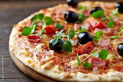 Pizza with ham, mozzarella cheese, cherry tomatoes, black olives and fresh oregano. Home made food. Concept for a tasty and hearty meal. Rustic wooden background. Close up. 