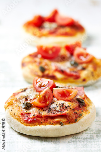 Obraz na płótnie Mini pizzas with ham, cherry tomatoes, mozzarella and capers on bright wooden background. Close up. 