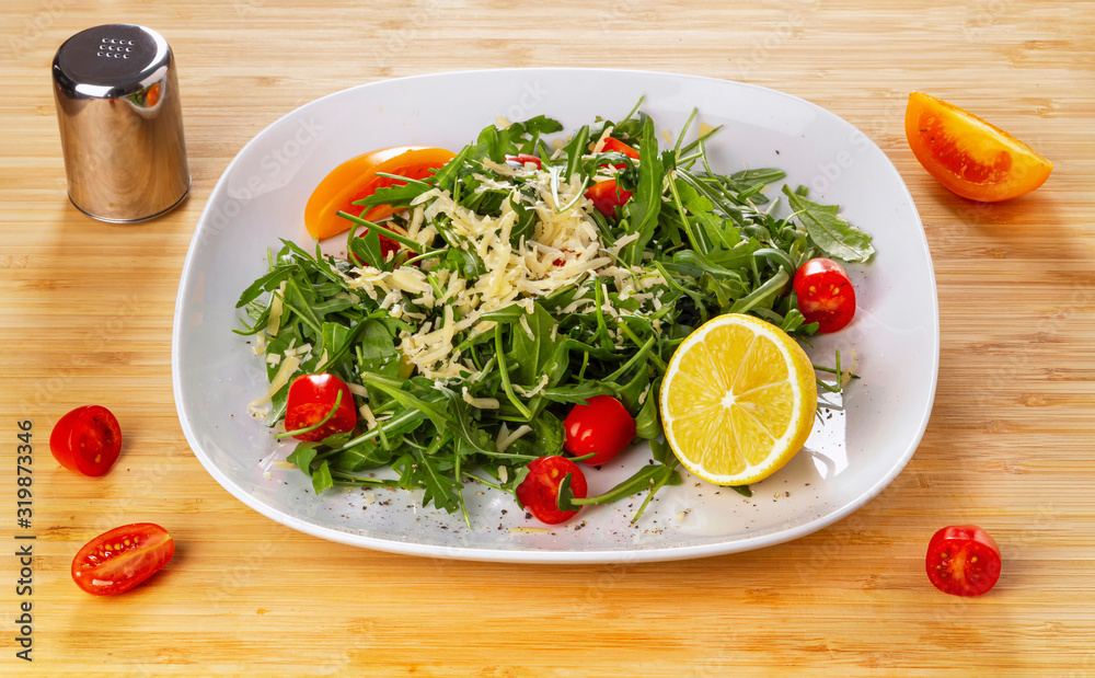 Arugula salad with cherry tomatoes and lemon on a white plate.