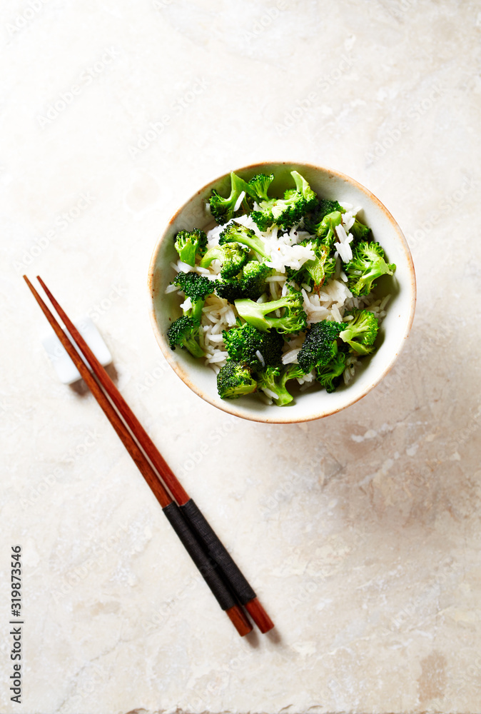 Cooked rice with fried broccoli on bright stone background. Top view.