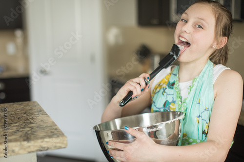 Young girl licking spatula while baking cake at home